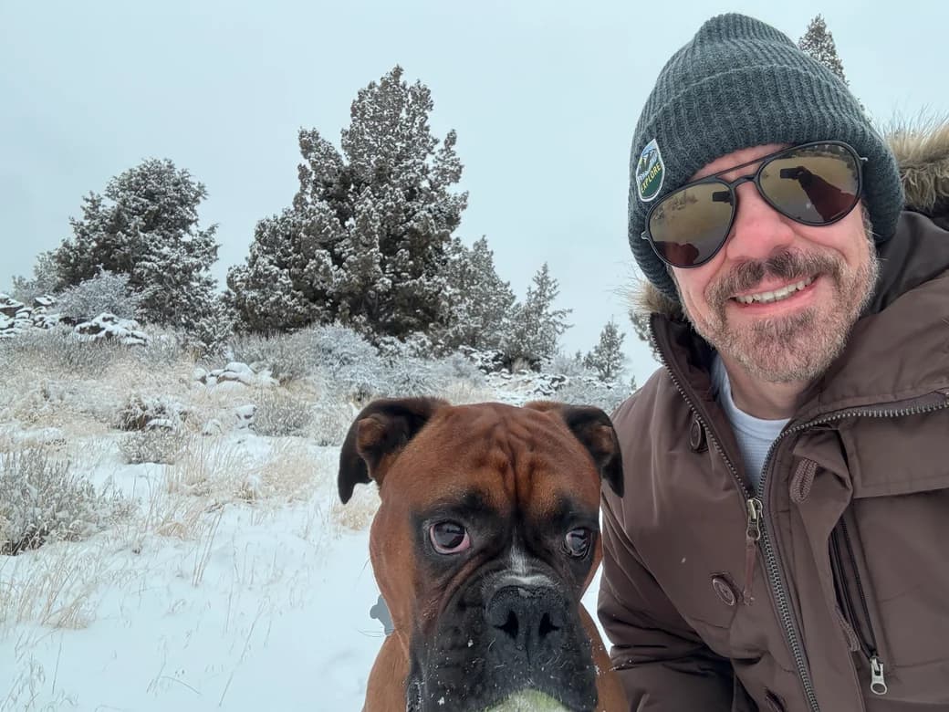 Adam Cagle on the right, smiling beside his dog Archer in a snowy landscape